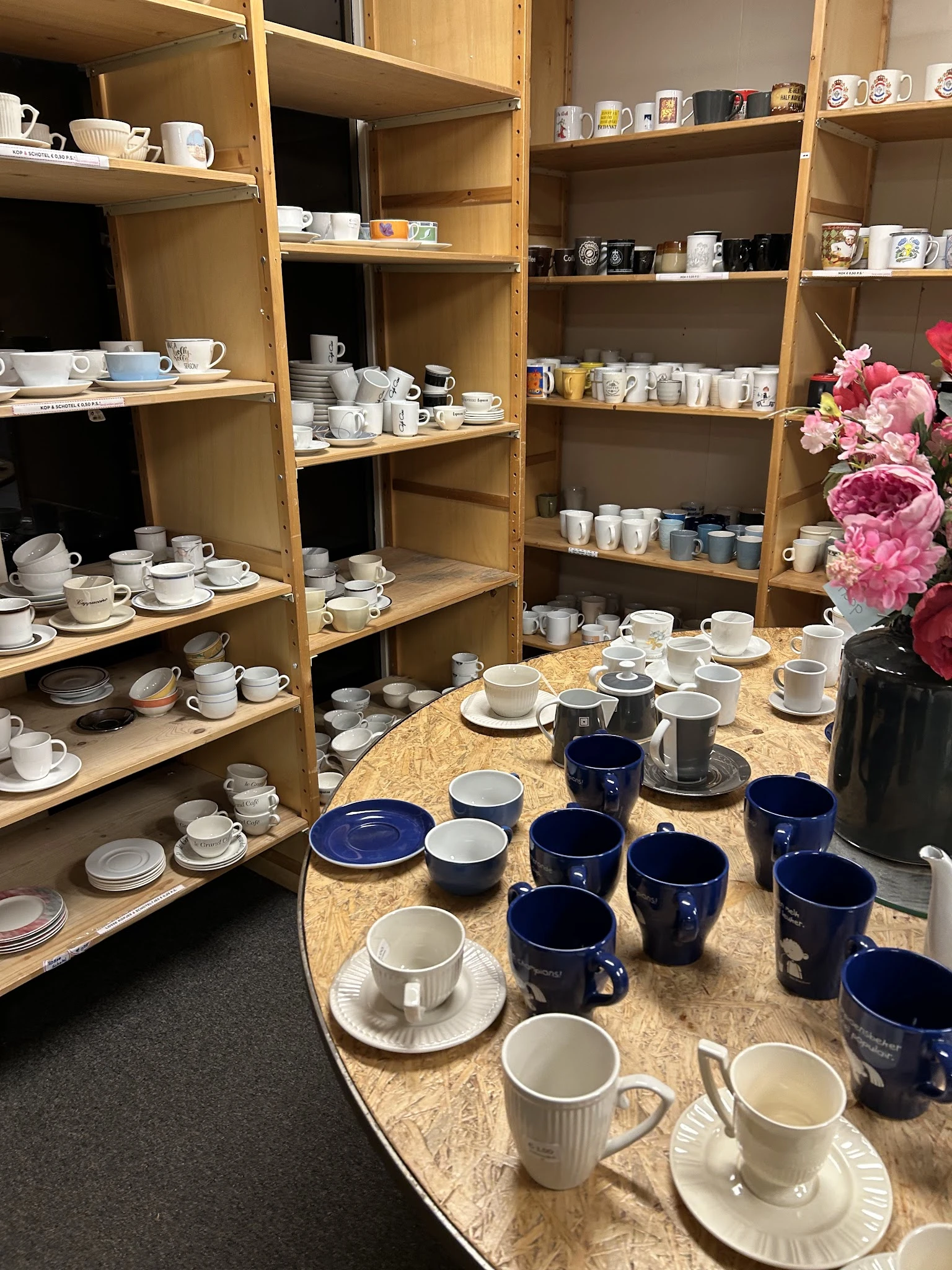 Uitgestalde serviesgoed en kopjes op tafel en houten stellingen in de winkel