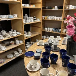 Uitgestalde serviesgoed en kopjes op tafel en houten stellingen in de winkel