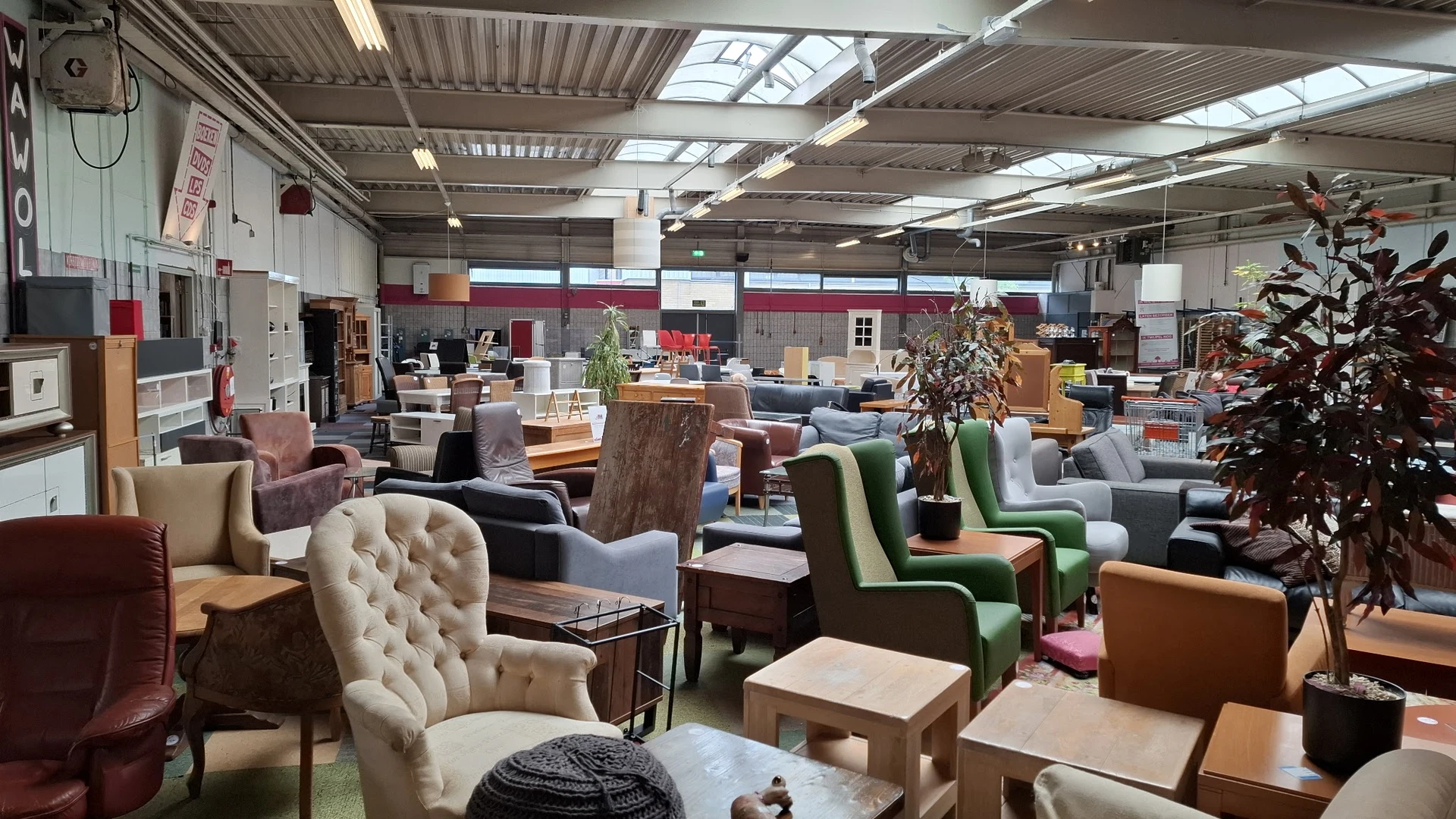 Winkelvloer met diverse tweedehands meubels: fauteuils, stoelen en tafels uitgestald in een ruim magazijninterieur.