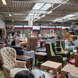 Winkelvloer met diverse tweedehands meubels: fauteuils, stoelen en tafels uitgestald in een ruim magazijninterieur.