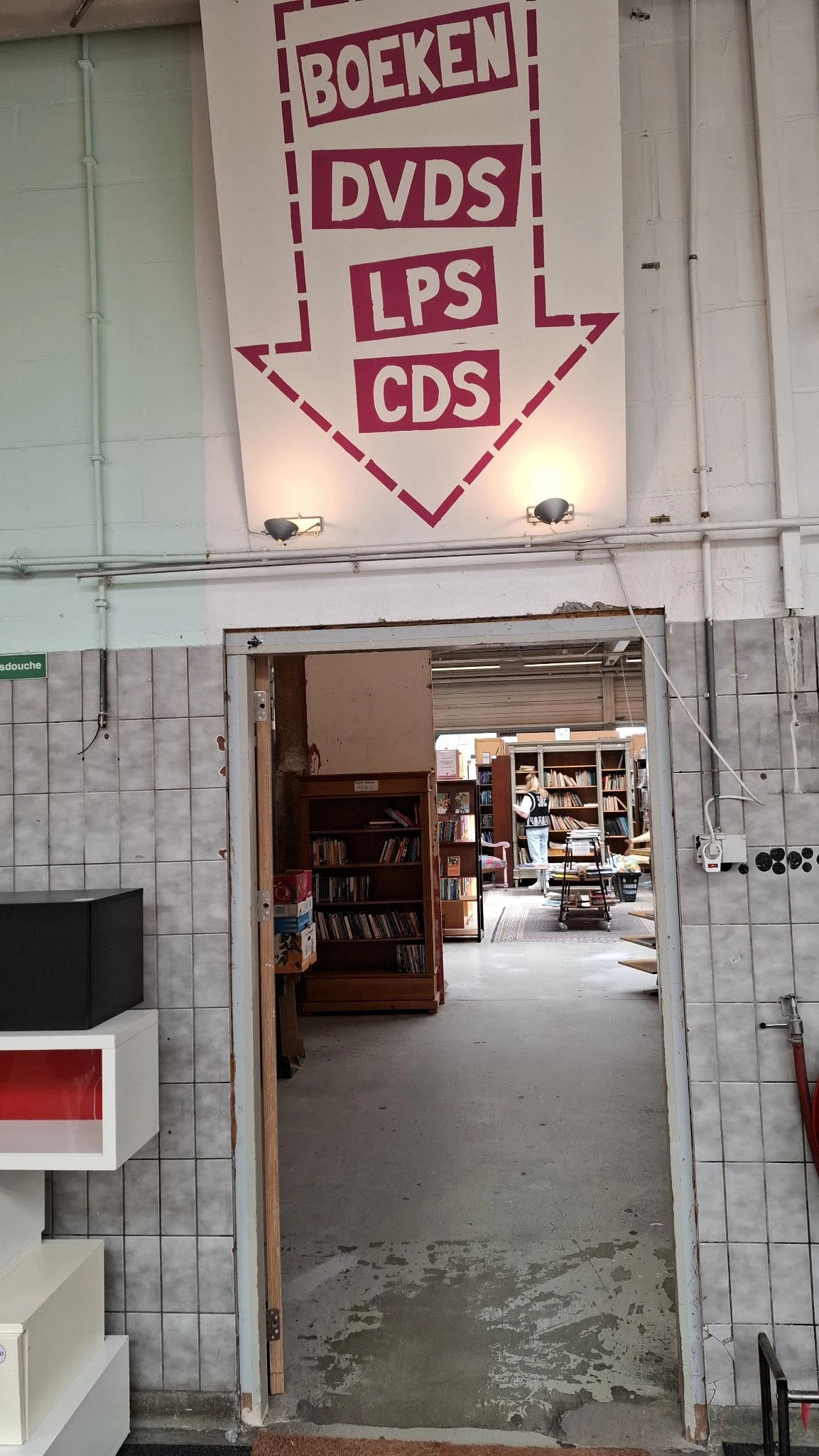 Binnenaanzicht van kringloopwinkel met boeken in houten kasten en doorgang naar volgende ruimte