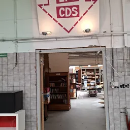 Binnenaanzicht van kringloopwinkel met boeken in houten kasten en doorgang naar volgende ruimte