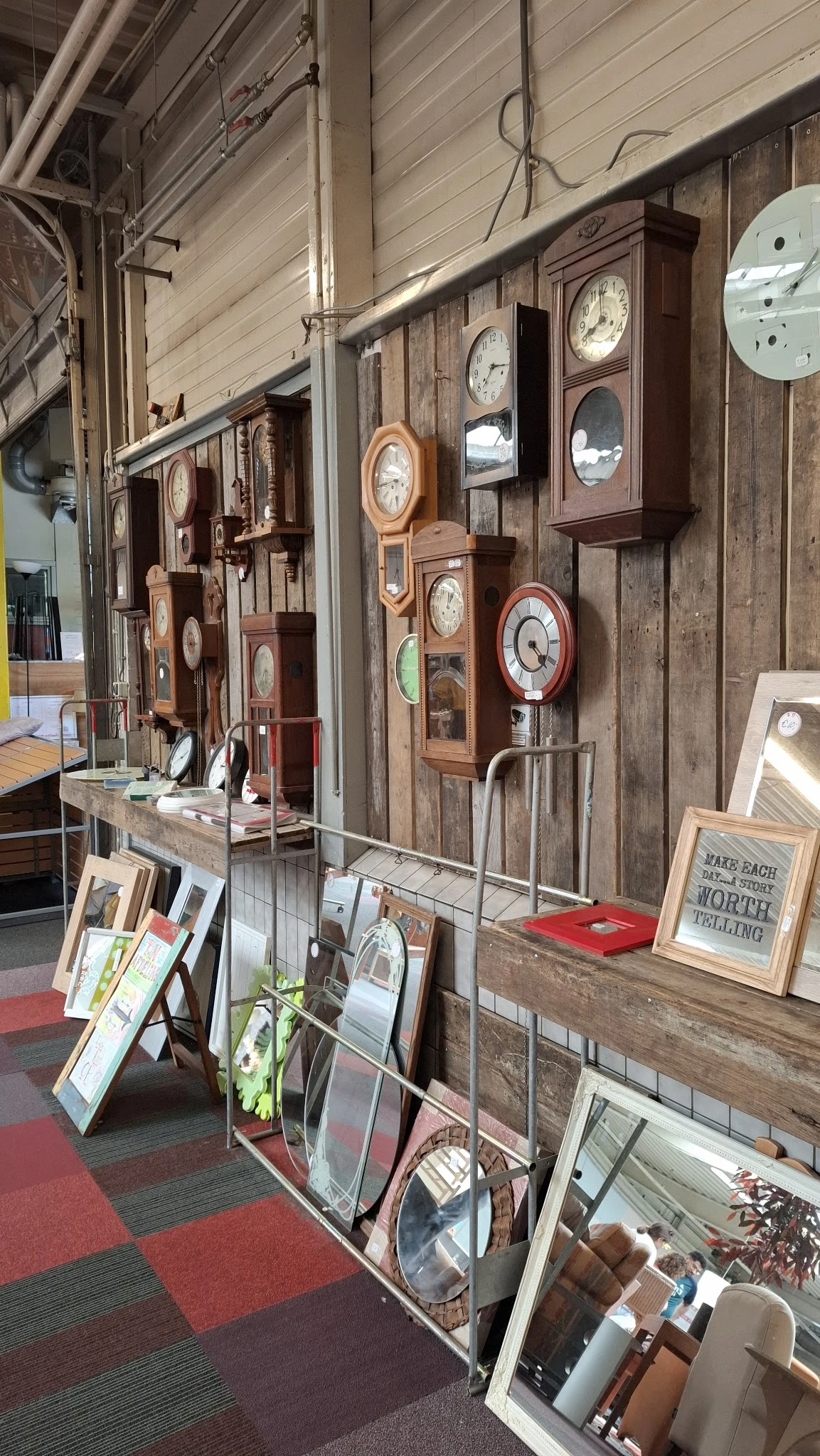 Wandklok verzameling met houten en rode klokken op houten paneel, onderaan display met boeken en decoratieve items