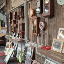 Wandklok verzameling met houten en rode klokken op houten paneel, onderaan display met boeken en decoratieve items