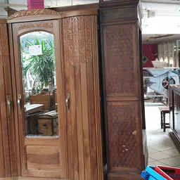 Houten kledingkast met spiegeldeuren en gebeeldhouwde details, in een kringloopwinkel