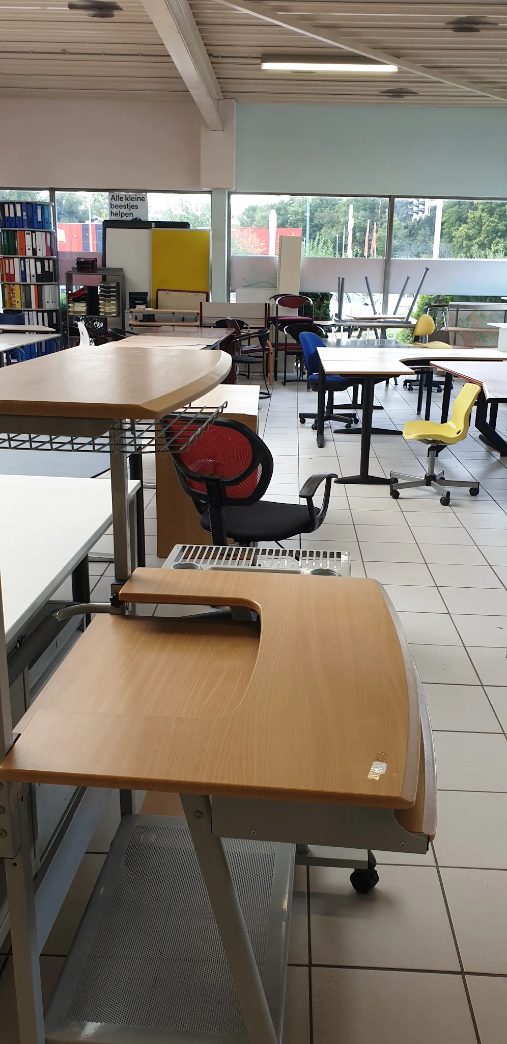 Winkelvloer met tafels, stoelen en een rode bureaustoel in een kringloopwinkel
