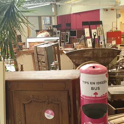 Overzicht van kringloopwinkel met meubels, kastjes, een grote schaal en plantje