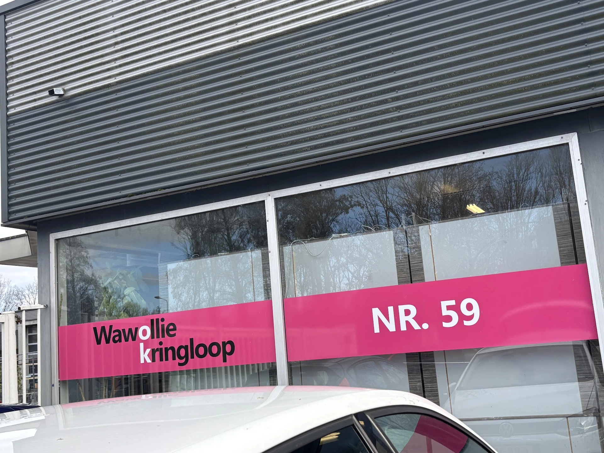 Winkelpui met grote ramen en roze banner met winkelnaam en adres