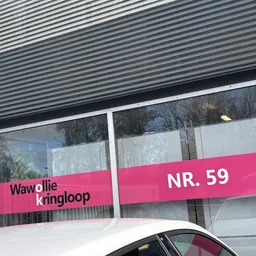 Winkelpui met grote ramen en roze banner met winkelnaam en adres