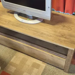 Houten tv-meubel met open vak en gesloten laden, met een witte JVC-televisie erop