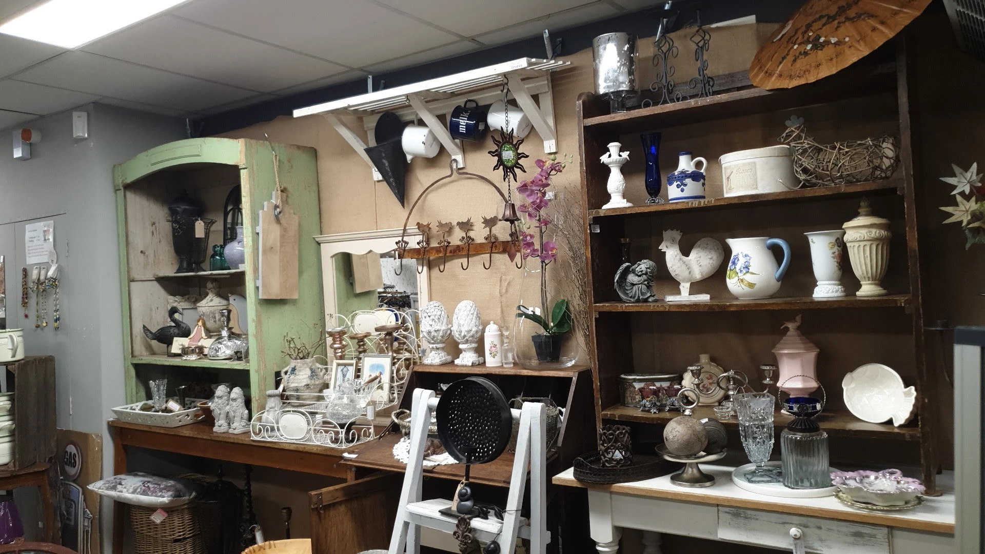 Uitgestalde vintage en antieke spullen op schappen en werktafels, waaronder servies, decoratie, lampen en diverse huishoudart