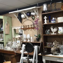 Uitgestalde vintage en antieke spullen op schappen en werktafels, waaronder servies, decoratie, lampen en diverse huishoudart