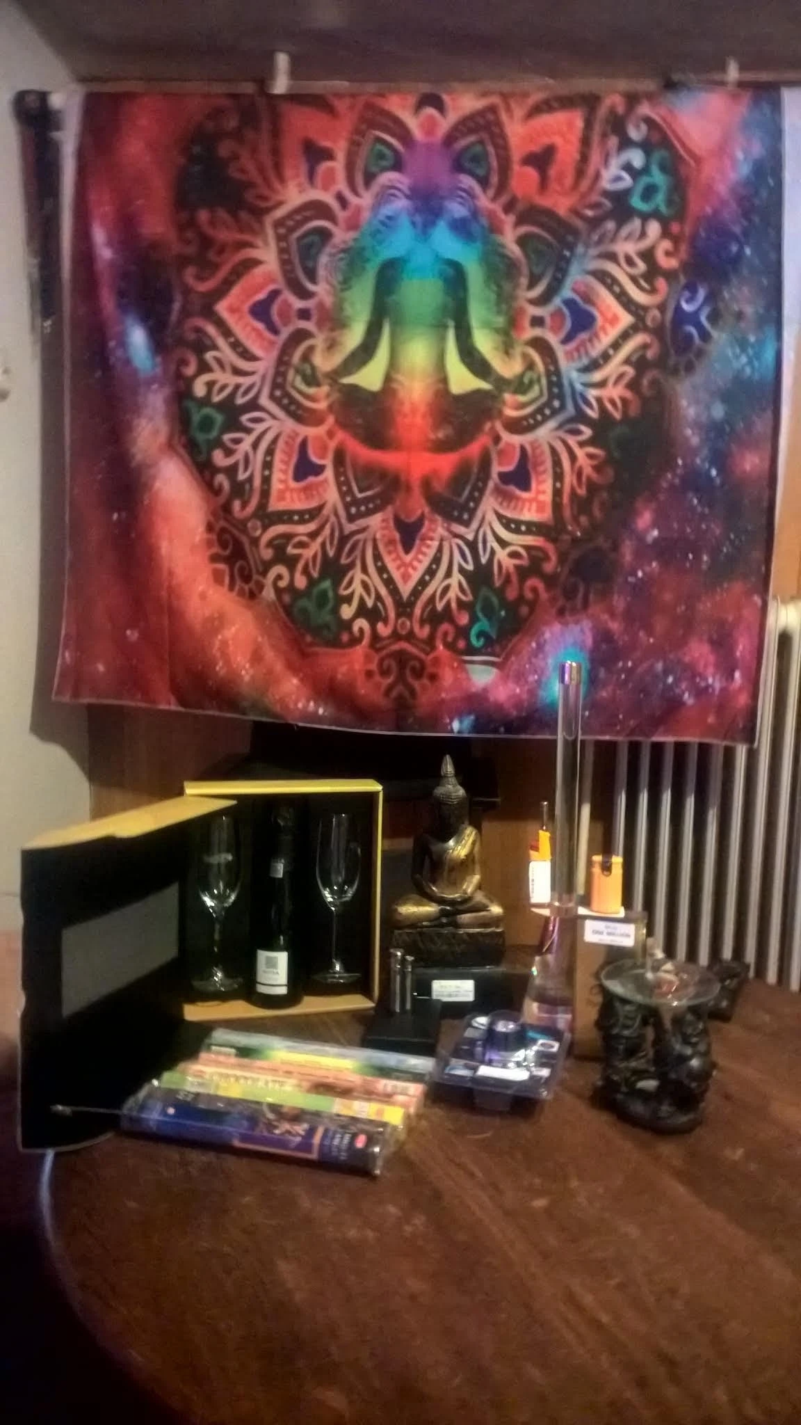 Uitgestald assortiment met fles wijn, glazen, boeddhabeeld en kandelaar tegen achtergrond met mandala-motief