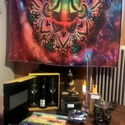 Uitgestald assortiment met fles wijn, glazen, boeddhabeeld en kandelaar tegen achtergrond met mandala-motief