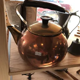 Glanzende koperen theepot met zwart deksel en handvat op houten tafel