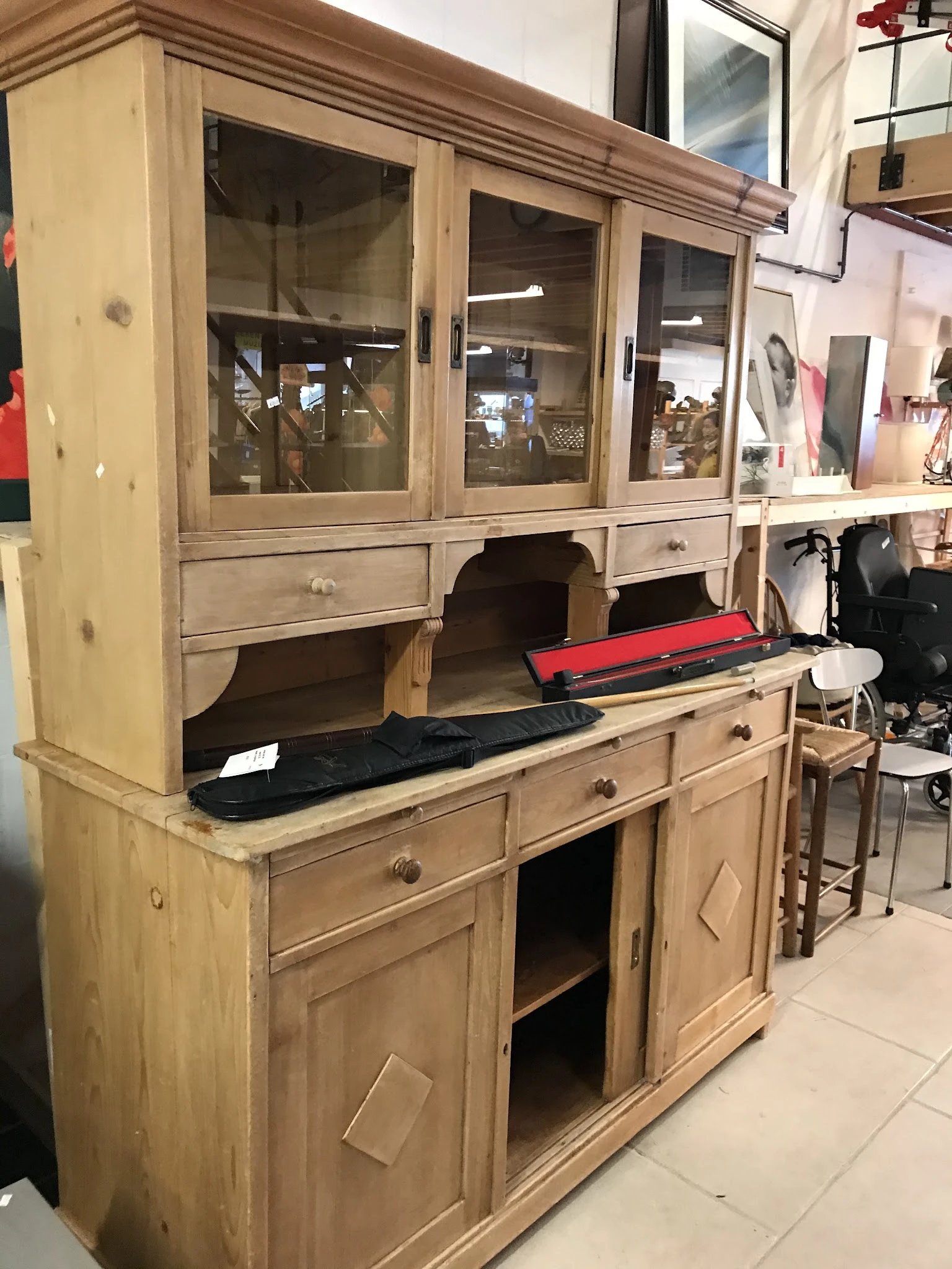 Houten buffetkast met glasdeuren, beladen met kleding en spullen in een kringloopwinkel