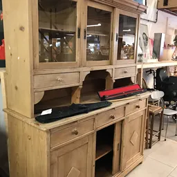 Houten buffetkast met glasdeuren, beladen met kleding en spullen in een kringloopwinkel