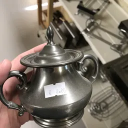 Zilveren tinnen suikerpot met deksel en oren, close-up in hand