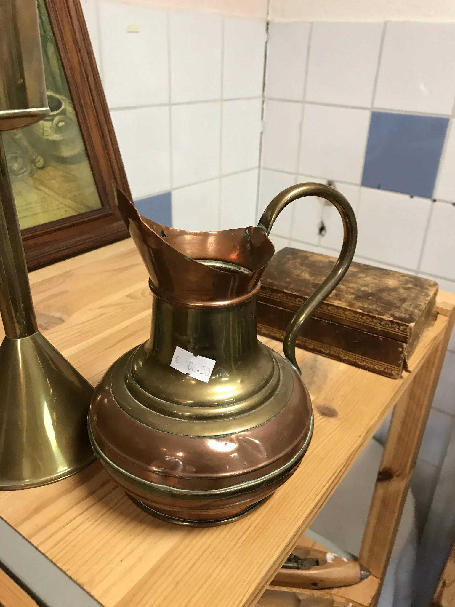 Koperen kan of kruik met gebogen oor op houten plank in de winkel