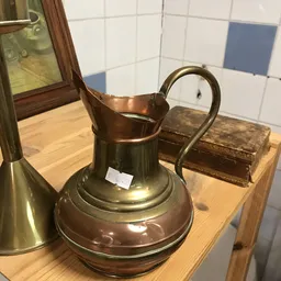 Koperen kan of kruik met gebogen oor op houten plank in de winkel