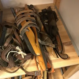 Verzameling oude riemen en zadels op houten ondergrond, waaronder bruin leer en metalen gespen