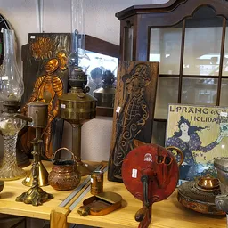 Vitrinekast met antieke en vintage objecten: gouden beeldjes, koperen lantaarns, glazen karaf, rode handschoenen, dartbord en