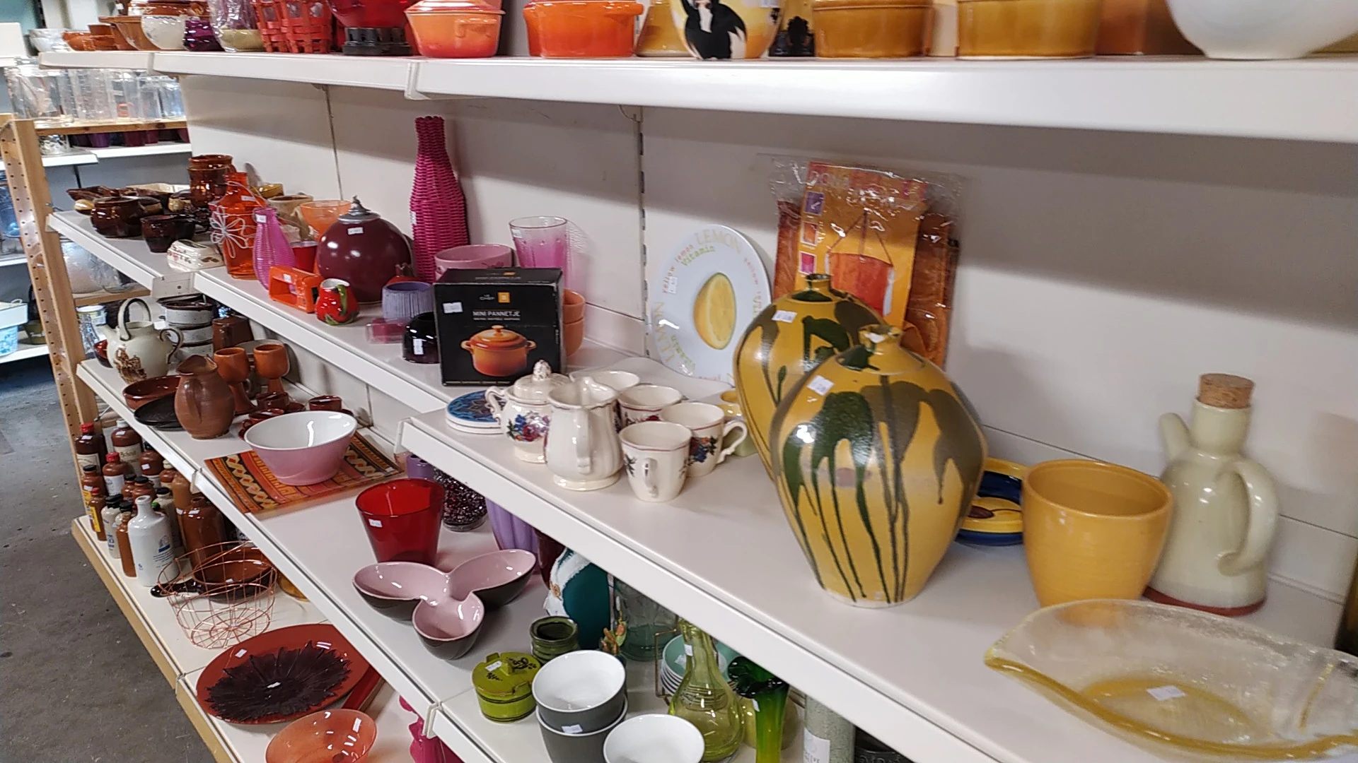 Schappen met uitgestalde serviesgoed, glazen, kannen en huishoudartikelen in verschillende kleuren