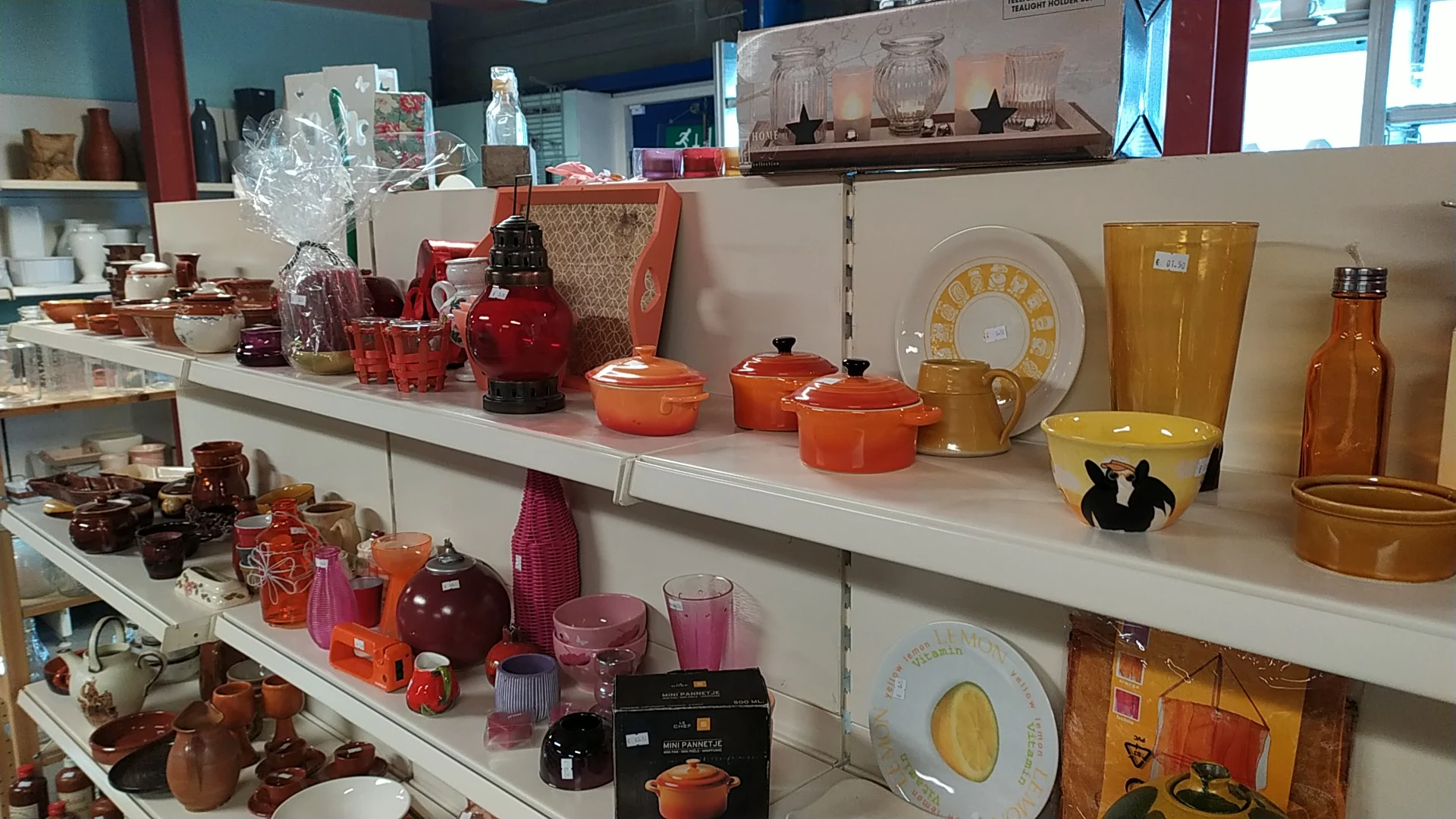 Witte stellingen met uitgestalde serviesgoed, pannen en keramiek in oranje, rood en geel