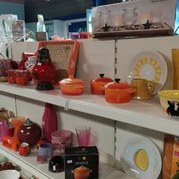 Witte stellingen met uitgestalde serviesgoed, pannen en keramiek in oranje, rood en geel