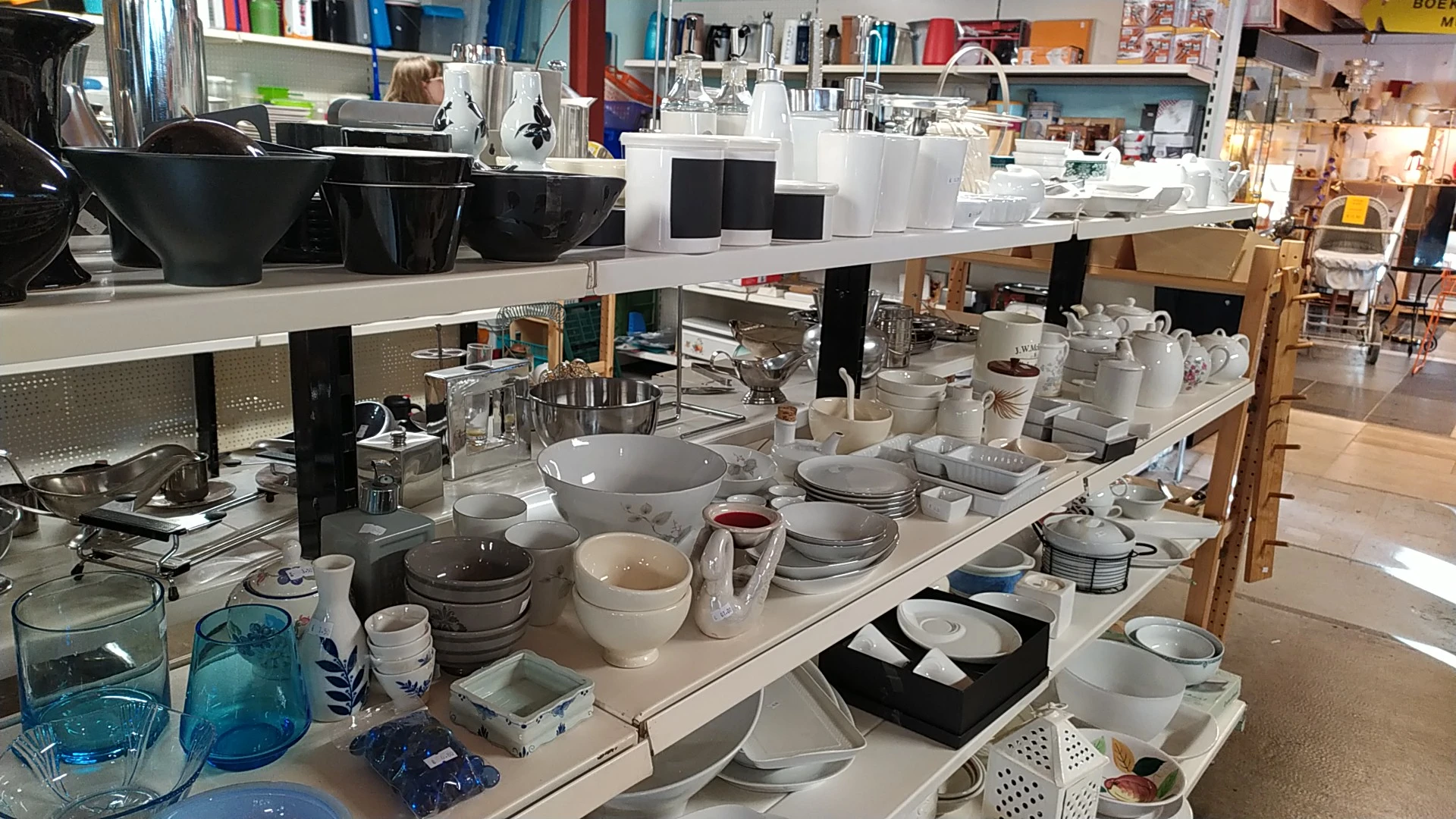 Tafel vol serviesgoed, schalen, borden en huishoudartikelen in een kringloopwinkel