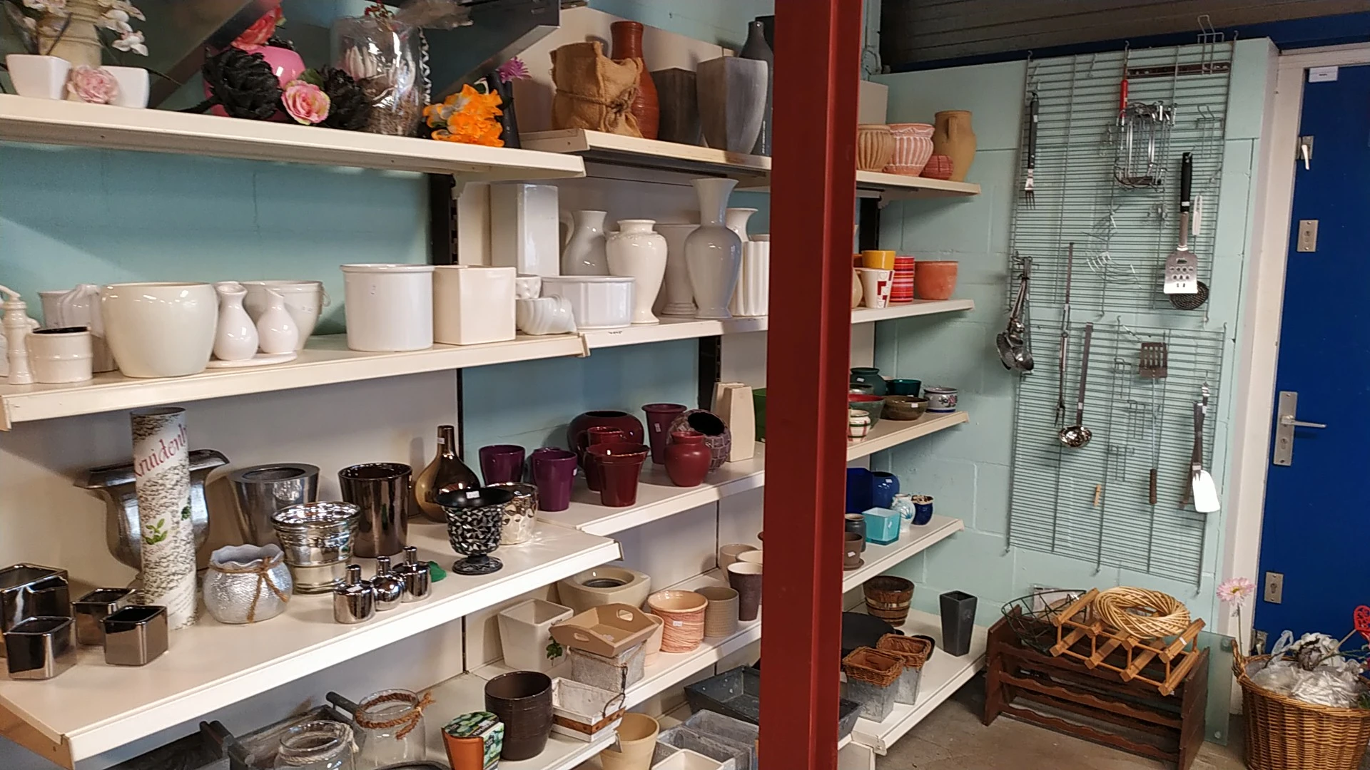 Witte en gekleurde huishoudelijke artikelen en decoratie op witte stellingen, waaronder vazen, kaarsen, glazen en decoratieve
