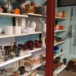 Witte en gekleurde huishoudelijke artikelen en decoratie op witte stellingen, waaronder vazen, kaarsen, glazen en decoratieve