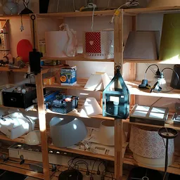 Houten stellingsysteem met diverse items zoals lampen, dozen, stoelen en huishoudelijke spullen in een kringloopwinkel
