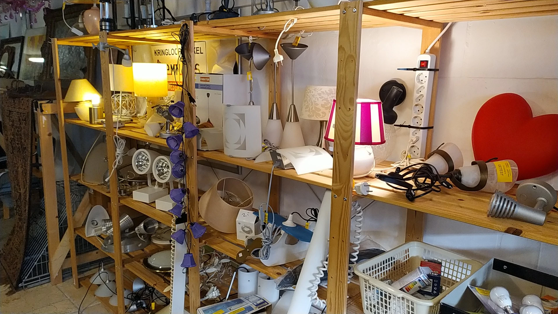 Houten stellingen volgestouwd met huishoudelijke apparaten, lampen en diverse tweedehands spullen