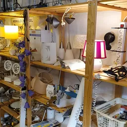Houten stellingen volgestouwd met huishoudelijke apparaten, lampen en diverse tweedehands spullen