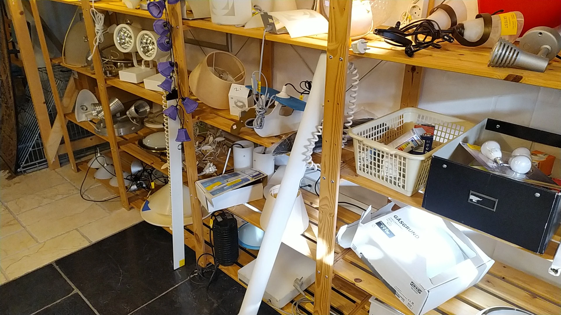 Houten stellingen vol met huishoudelijke items, elektrische apparaten en ander assortiment in een kringloopwinkel