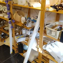 Houten stellingen vol met huishoudelijke items, elektrische apparaten en ander assortiment in een kringloopwinkel