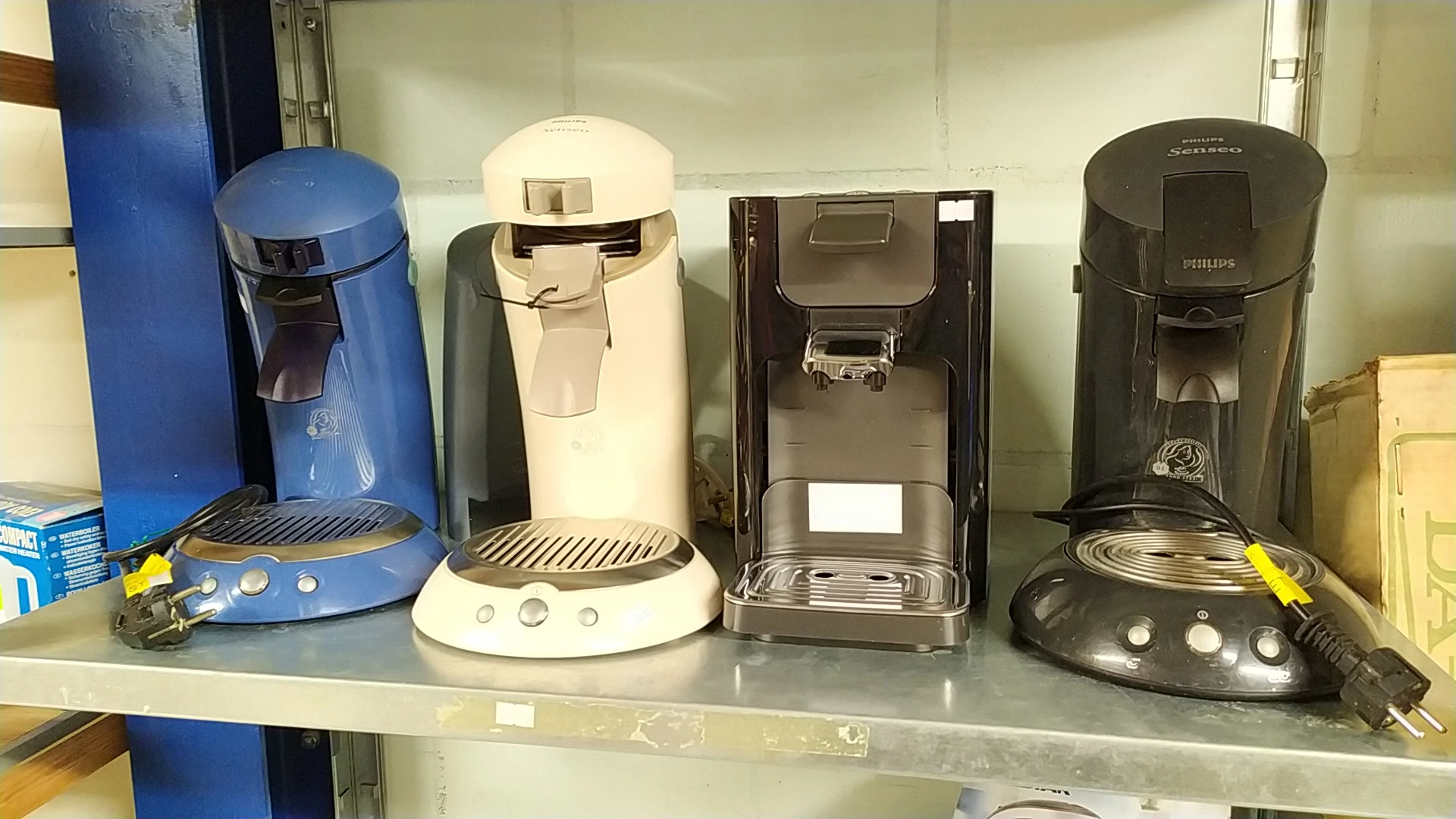 Vijf koffiezetapparaten in verschillende kleuren en modellen op een winkelplank