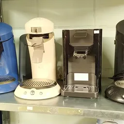 Vijf koffiezetapparaten in verschillende kleuren en modellen op een winkelplank
