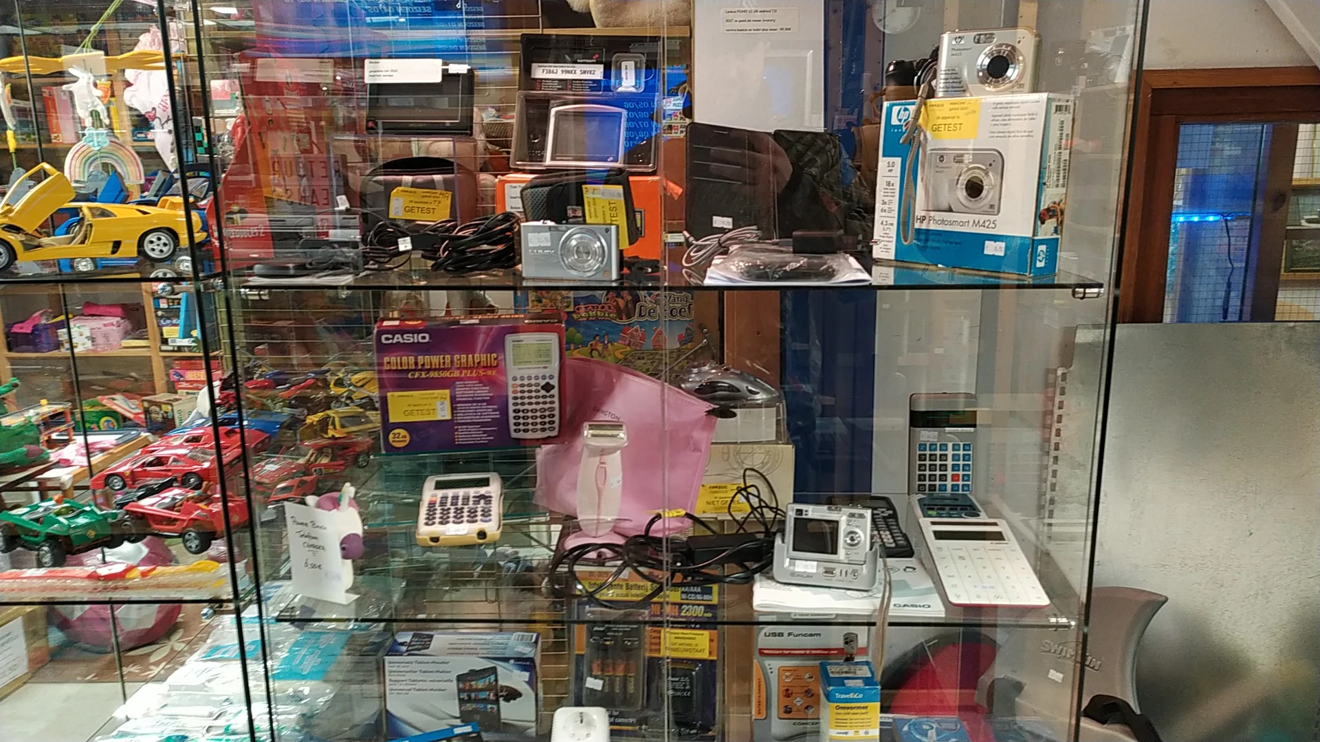 Glazen vitrinekast met elektronische apparaten: rekenmachines, digitale camera's, wasmachines en andere huishoudelijke artike