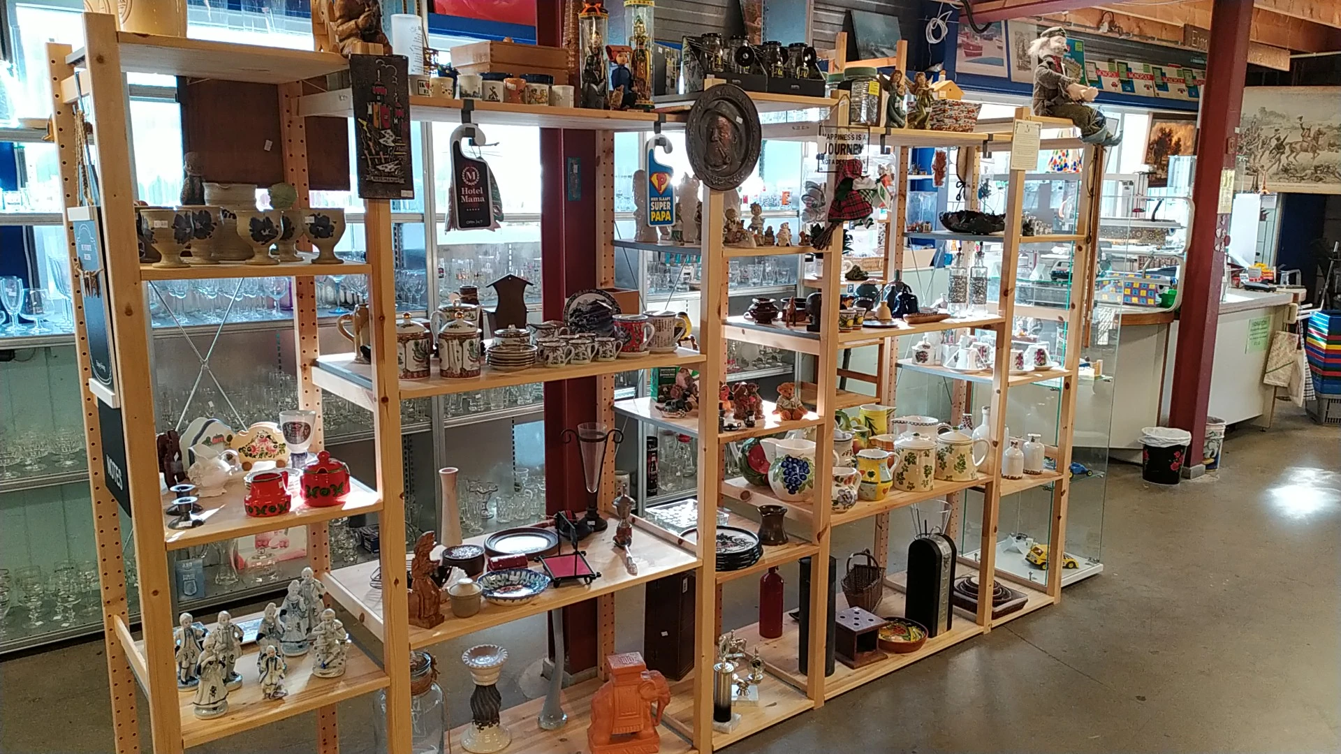 Houten vitrinekasten met uitgestalde decoratieve artikelen, servies, vazen en diverse tweedehandsartikelen in een kringloopwi