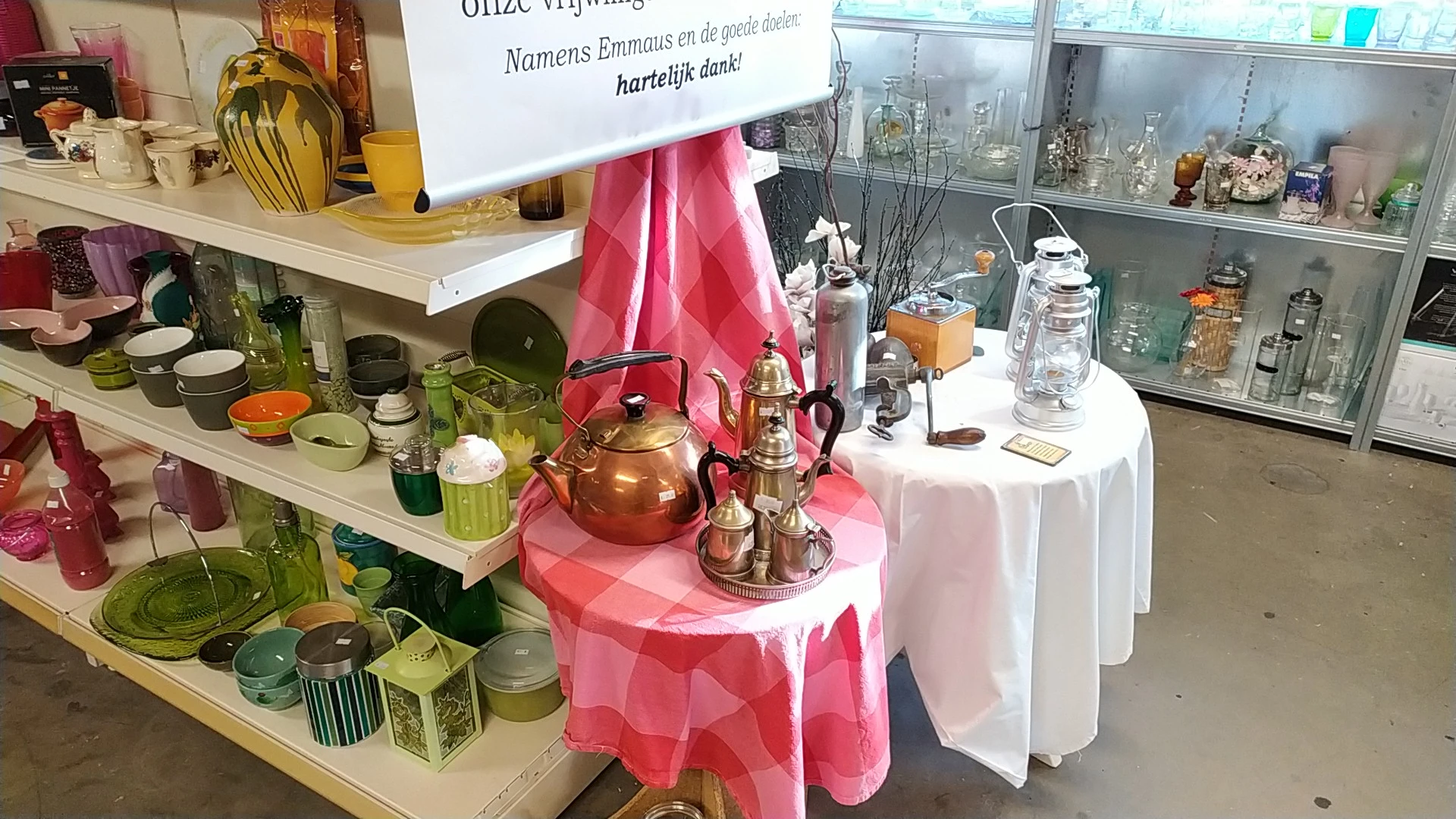 Vitrinekast met huishoudelijke artikelen: koperen theepot, glazen flessen, serviesgoed en decoratieve items op witte tafel me