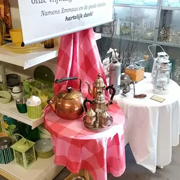 Vitrinekast met huishoudelijke artikelen: koperen theepot, glazen flessen, serviesgoed en decoratieve items op witte tafel me