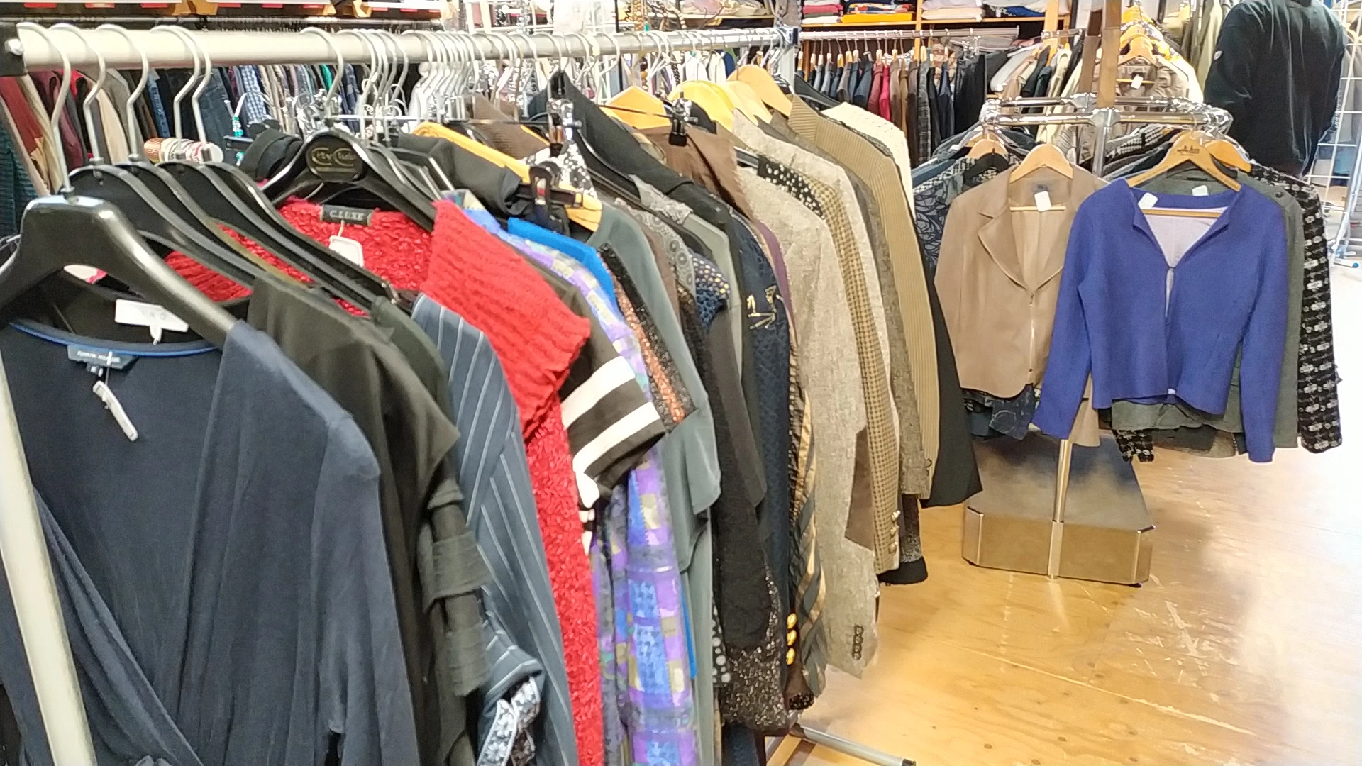 Rekken met tweedehands kleding op hangers, diverse kleuren en stijlen