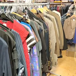 Rekken met tweedehands kleding op hangers, diverse kleuren en stijlen