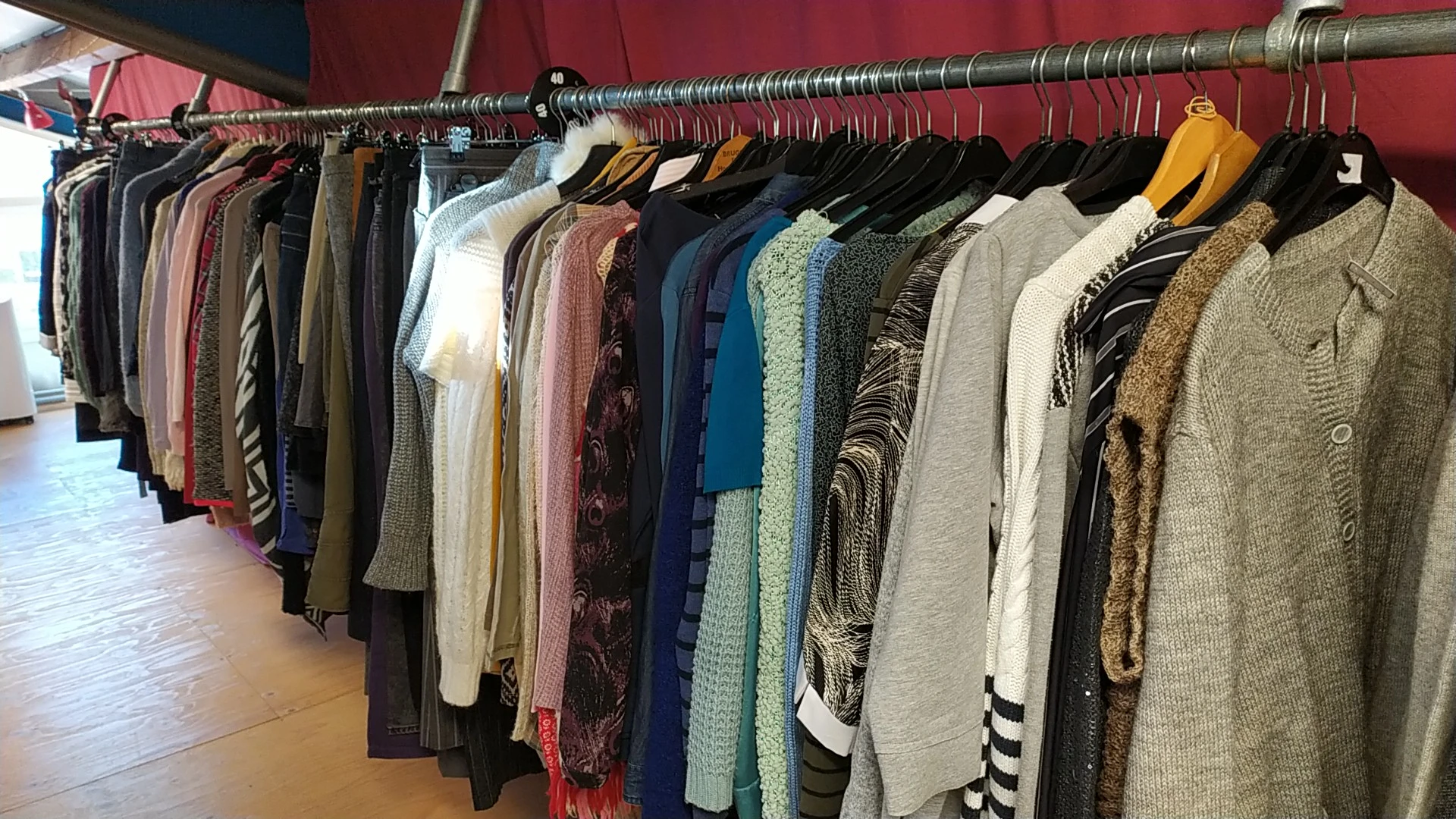Rekken met diverse tweedehands kleding in verschillende kleuren en stijlen op hangers