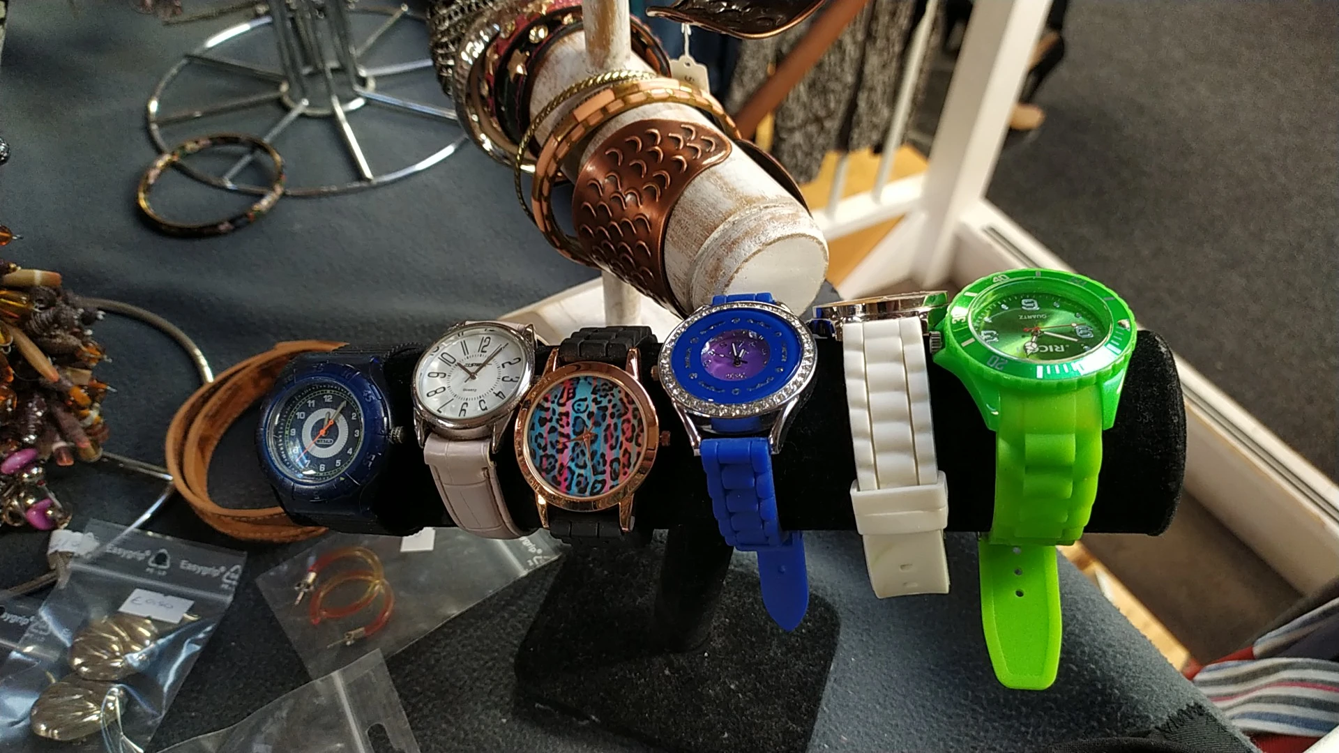 Zeven verschillende horloges uitgestald op een zwart display, waaronder digitale en analoge modellen in diverse kleuren