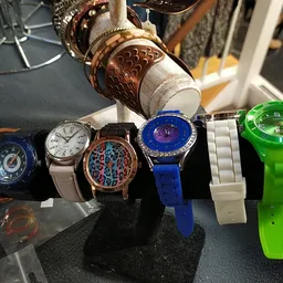 Zeven verschillende horloges uitgestald op een zwart display, waaronder digitale en analoge modellen in diverse kleuren