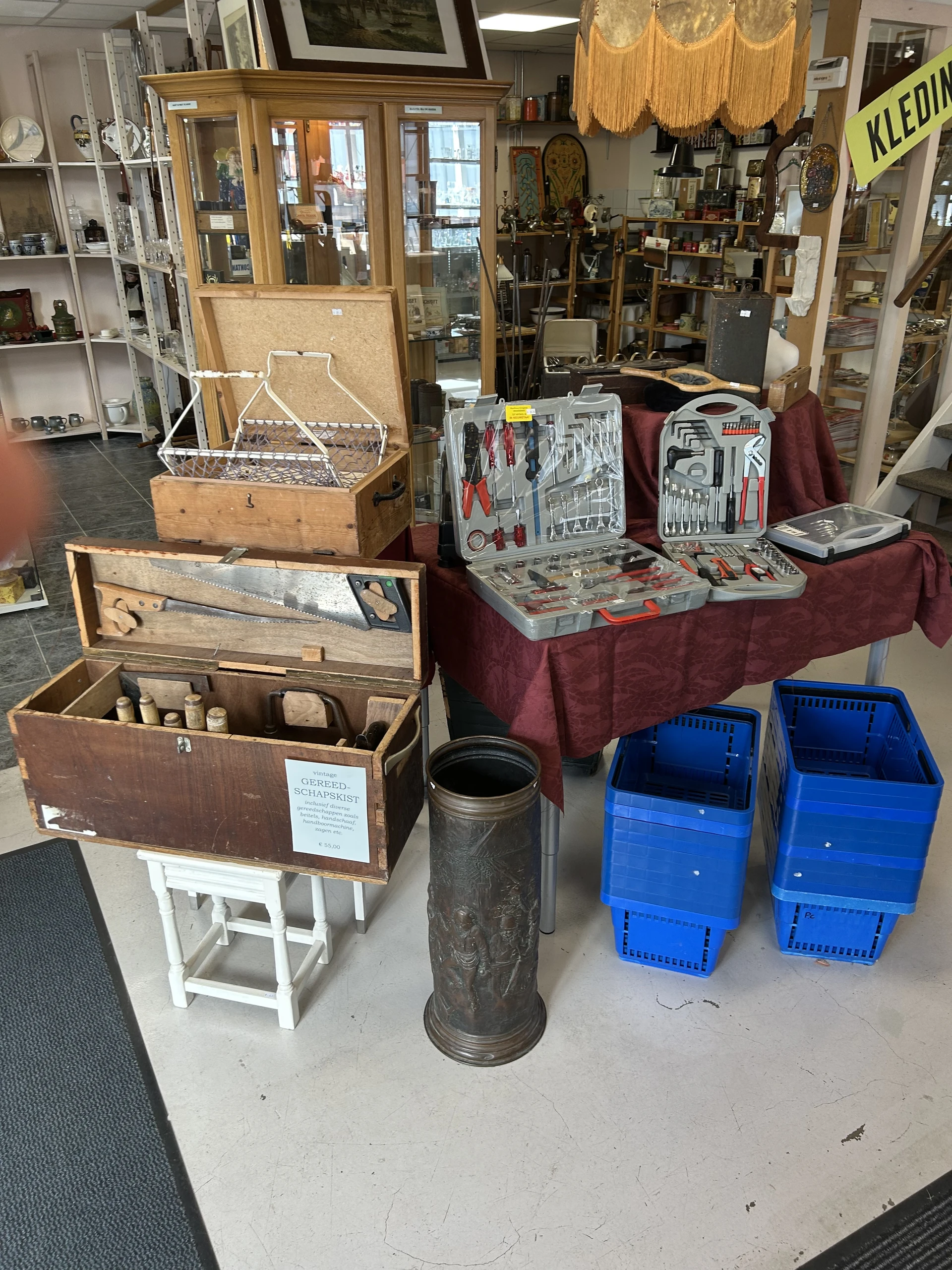 Uitgestalde tweedehands gereedschapssetjes, toolboxen en blauwe kunststofkratjes in een kringloopwinkel