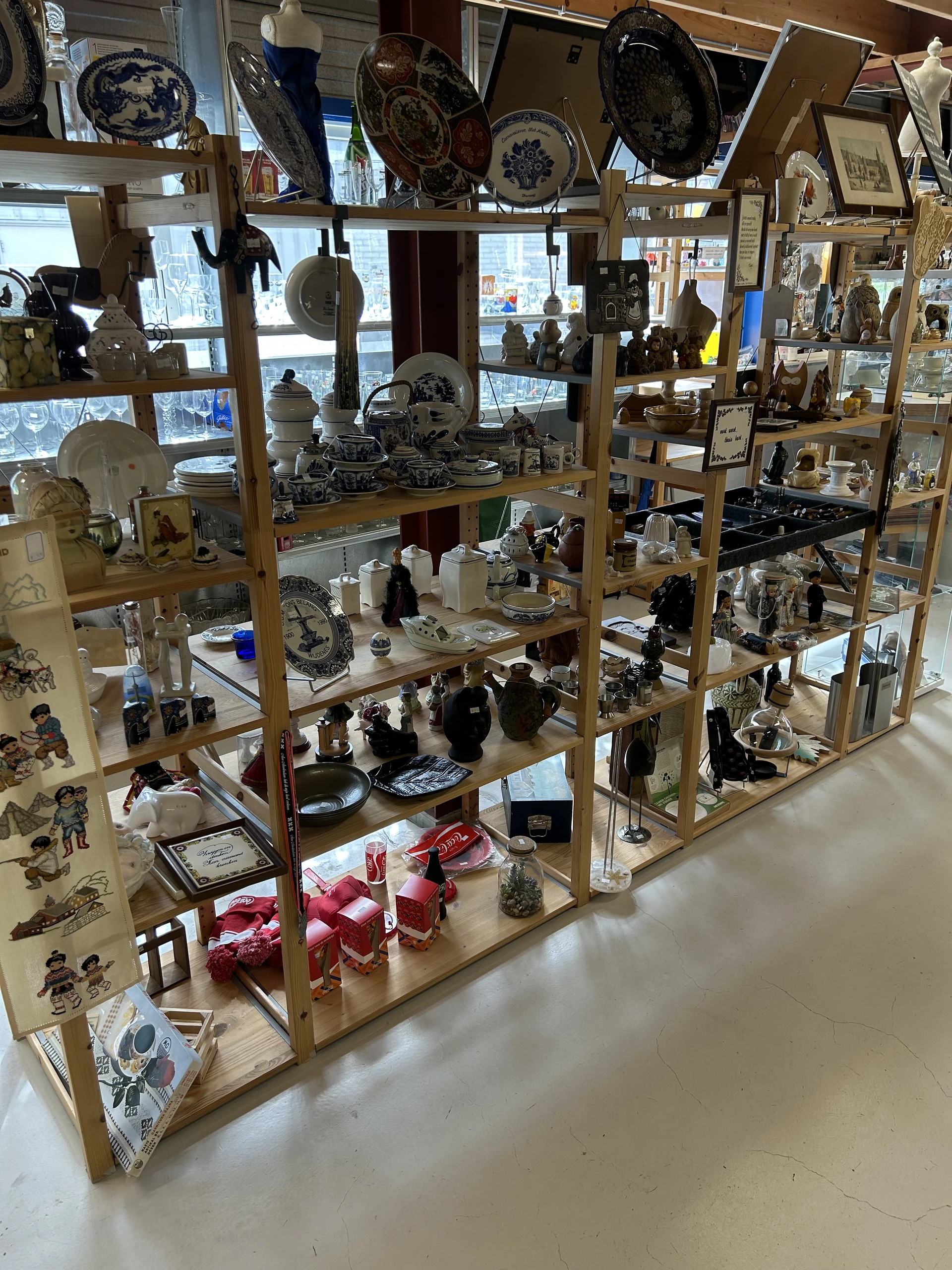 Houten stellingkast gevuld met diverse tweedehands huisraad, servies, beeldjes en decoratieve voorwerpen
